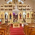 A view of iconostas and empty pews as seen from the back of the church. Pussy willows are on a table near the front, and the table has a white tablecloth. A man in a light blue shirt is also partially visible on the left side of the frame. He's up near the front of the church, and while I'm not sure what he's doing, my guess is that he was lighting candles before the start of the service.