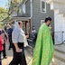 A view of the front part of a procession around the church. Father Aleksey is standing at the steps that lead into the church, and he's wearing a green vestment and carrying a gold cross. A line of parishioners, holding pussy willows, follow behind him, and the line leads around to the side of the church.