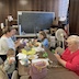 A group of parishioners sitting at a table in the church hall. They're working with scissors, and there's a pile of bows on the table along with bunches of pussy willows.