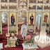 A photo similar to the previous photo but taken from a further left angle, and in this photo, Fr. Aleksey is presenting the Royal Gifts to the congregation. A man, who is wearing a peach-colored shirt and is holding a large candle, stands in from of the priest.