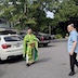 Photo of Fr. Aleksey standing with his back towards a white car. He is wearing a green and gold vestment and is facing a man who is wearing a grayish-blue shirt and black pants and appears on the right side of the frame.