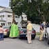 Photo of Fr. Aleksey blessing a black car. Two other cars and three people are visible in the frame. Two are watching the blessing and other is looking into an SUV at frame right..