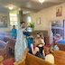 Using a bunch of basil dipped in holy water, Fr. Aleksey blesses two girls and a young boy who are standing in one of the pew at the back of the church. A beam of bluish light streams in from the out-of-view open door on the right, leading roughly to the basil, and a few beams of light stream in on the left, from out-of-view windows. The beams shine from middle left, leading to Fr. Aleksey's light blue vestments.