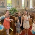 Fr. Aleksey's right arm appears in the middle left of the frame as he swings basil with which he is using to bless several young people. They are standing in the center aisle and in pews, towards the back of the church, and are laughing as they get spritzed with the holy water.