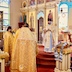 A clergy member holds a cross and is standing in front of the Royal Doors and is looking at three fellow clergy members who are facing him.