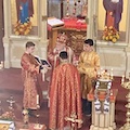 Close-up view, taken from the choir loft, of Archbishop Mark standing in front of the iconostas, and looking at a book that is being held by an altar server to his right. There's also an altar server to his right, and Fr. Aleksey is standing in front of Archbishop Mark.