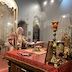 Archbishop Mark is standing in front of the altar table, looking to his left at a book that is sitting on a podium. His hand is resting on the book. The photo was taken from the back of the altar, and smoke from incense can be seen in the background through the royal archway. Beyond the smoke, a few pews and parishoners are also visible in the body of the church.